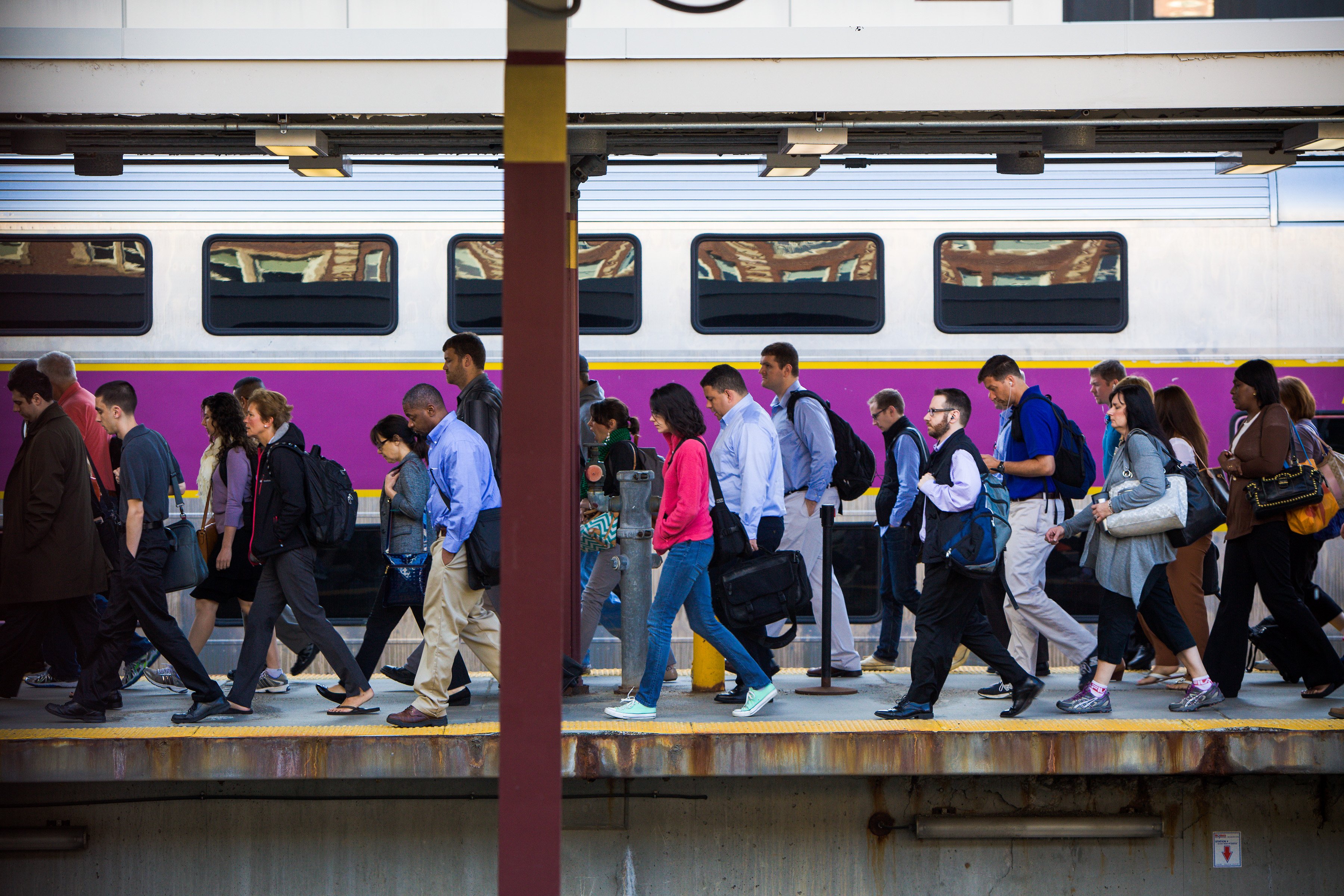 Passengers walk on a platform next to a Commuter Rail train