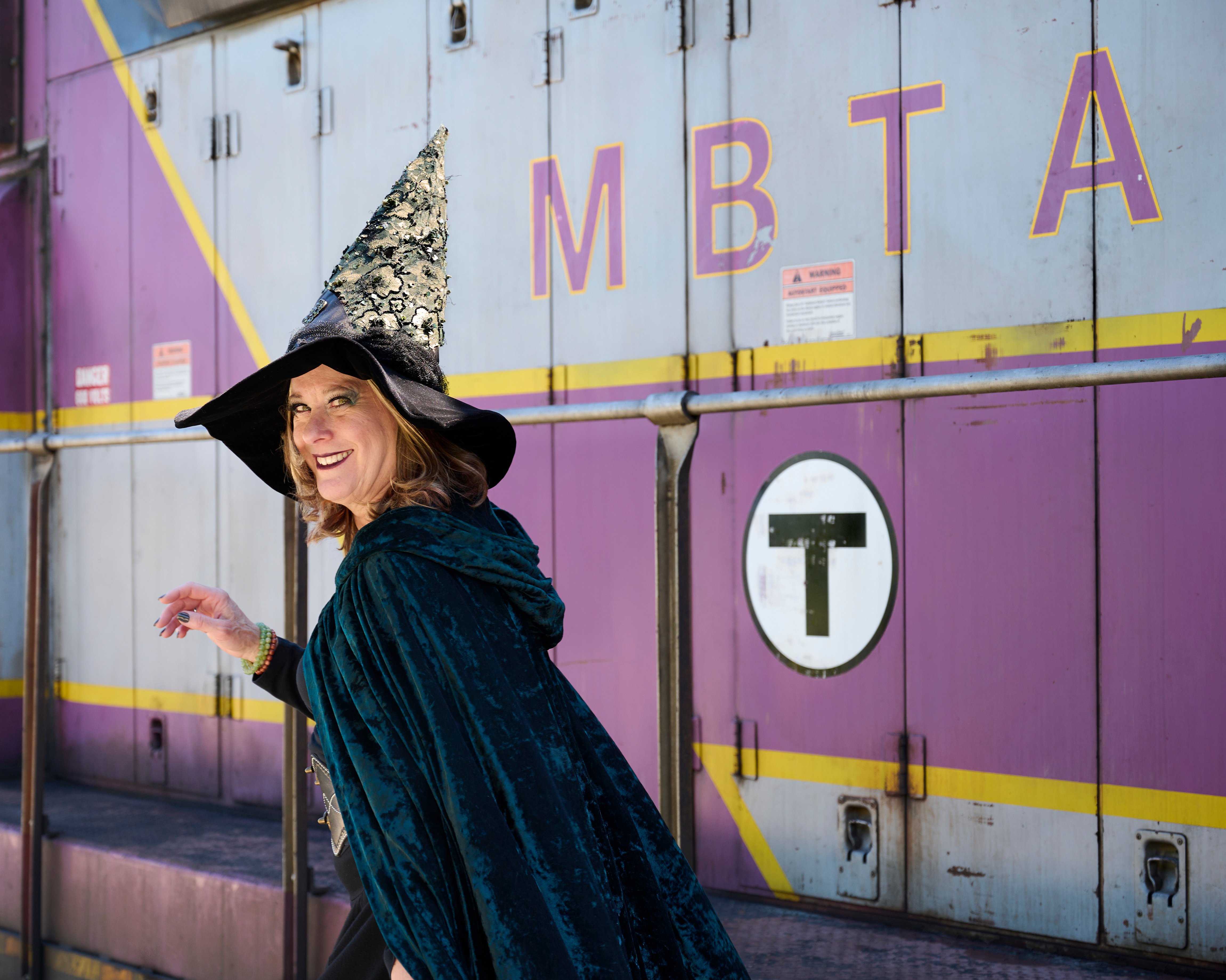 A person dressed as a witch in front of an MBTA train